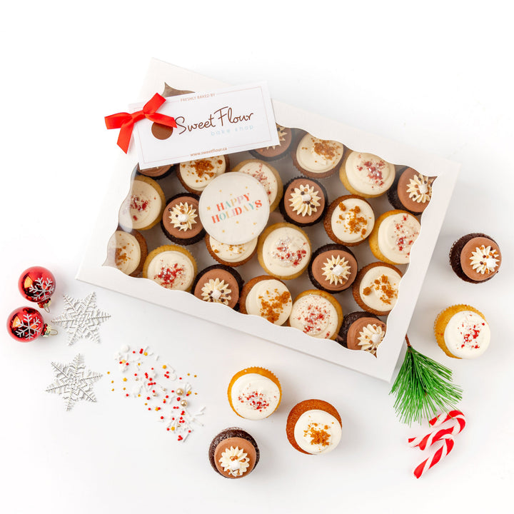 Box of mini cupcakes with decorative holiday elements on a white background
