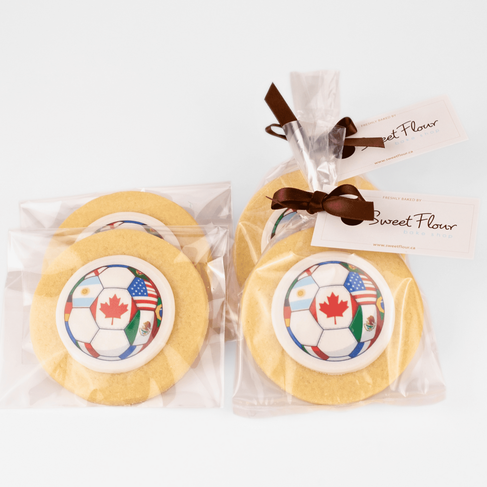 World Cup sugar cookies with a soccer ball design and Canadian flag, wrapped in clear plastic with a brown ribbon and 'Sweet Flour' tag.