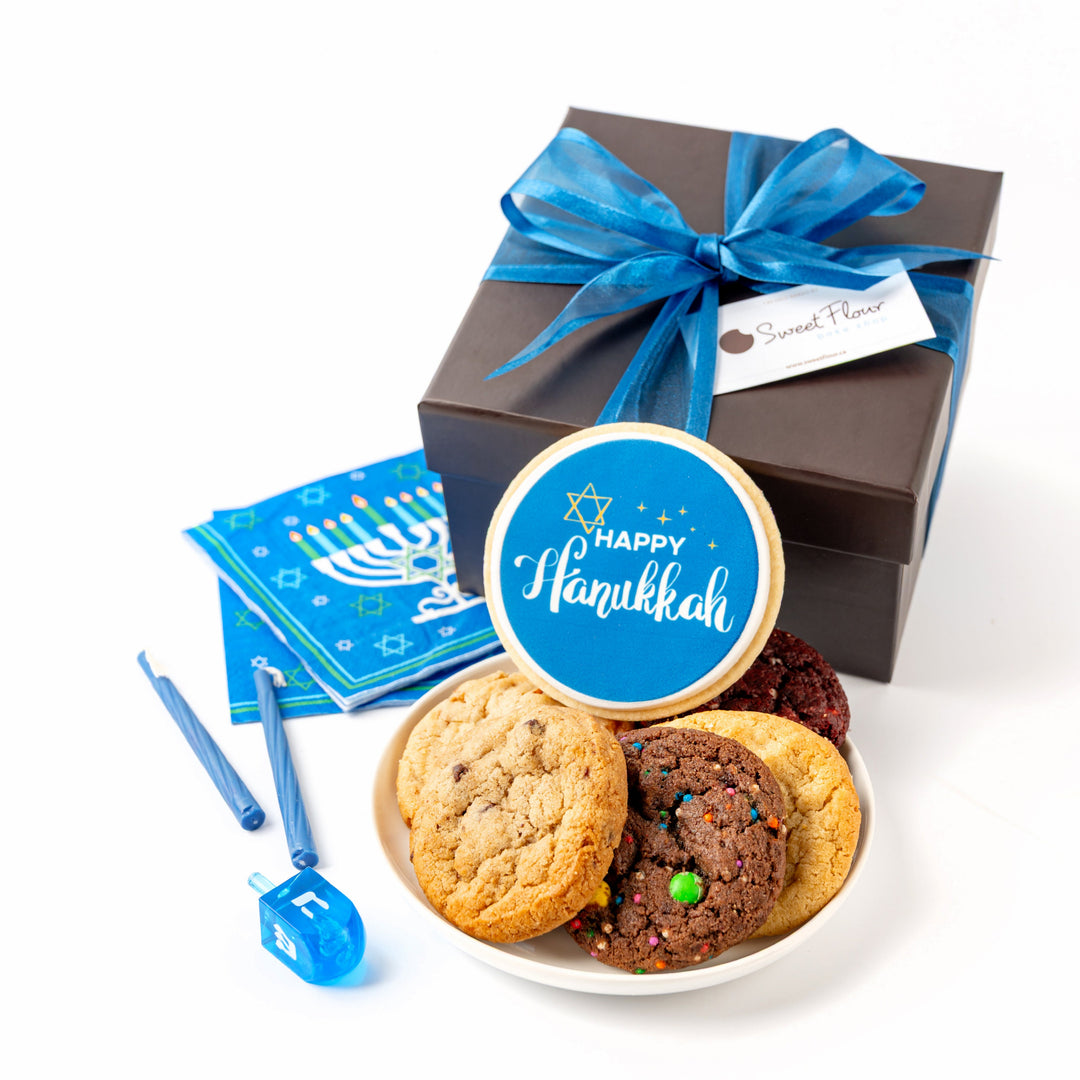 Gift box with blue ribbon, cookies, and Hanukkah-themed items on a white background
