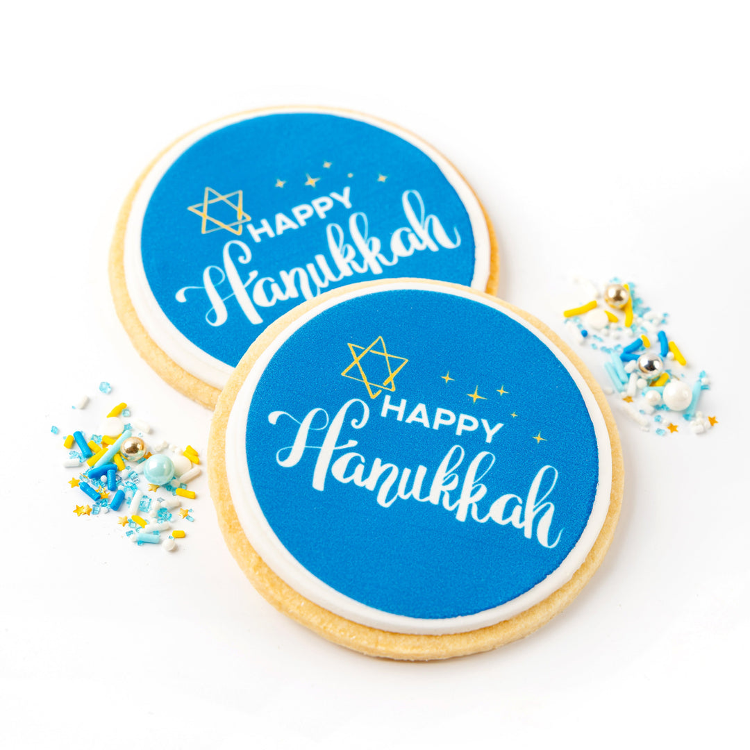 Two cookies with 'Happy Hanukkah' text on blue circles, surrounded by colorful sprinkles on a white background.