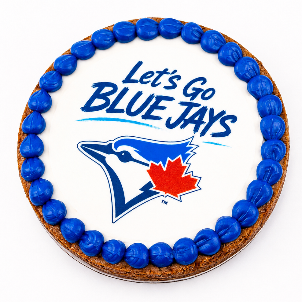 A round cake decorated with white icing, a border of blue candies, and the text 'Let's Go BLUE JAYS' above the Blue Jays logo with a red maple leaf. The cake is photographed from above on a clean white background.