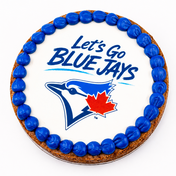 A round cake decorated with white icing, a border of blue candies, and the text 'Let's Go BLUE JAYS' above the Blue Jays logo with a red maple leaf. The cake is photographed from above on a clean white background.