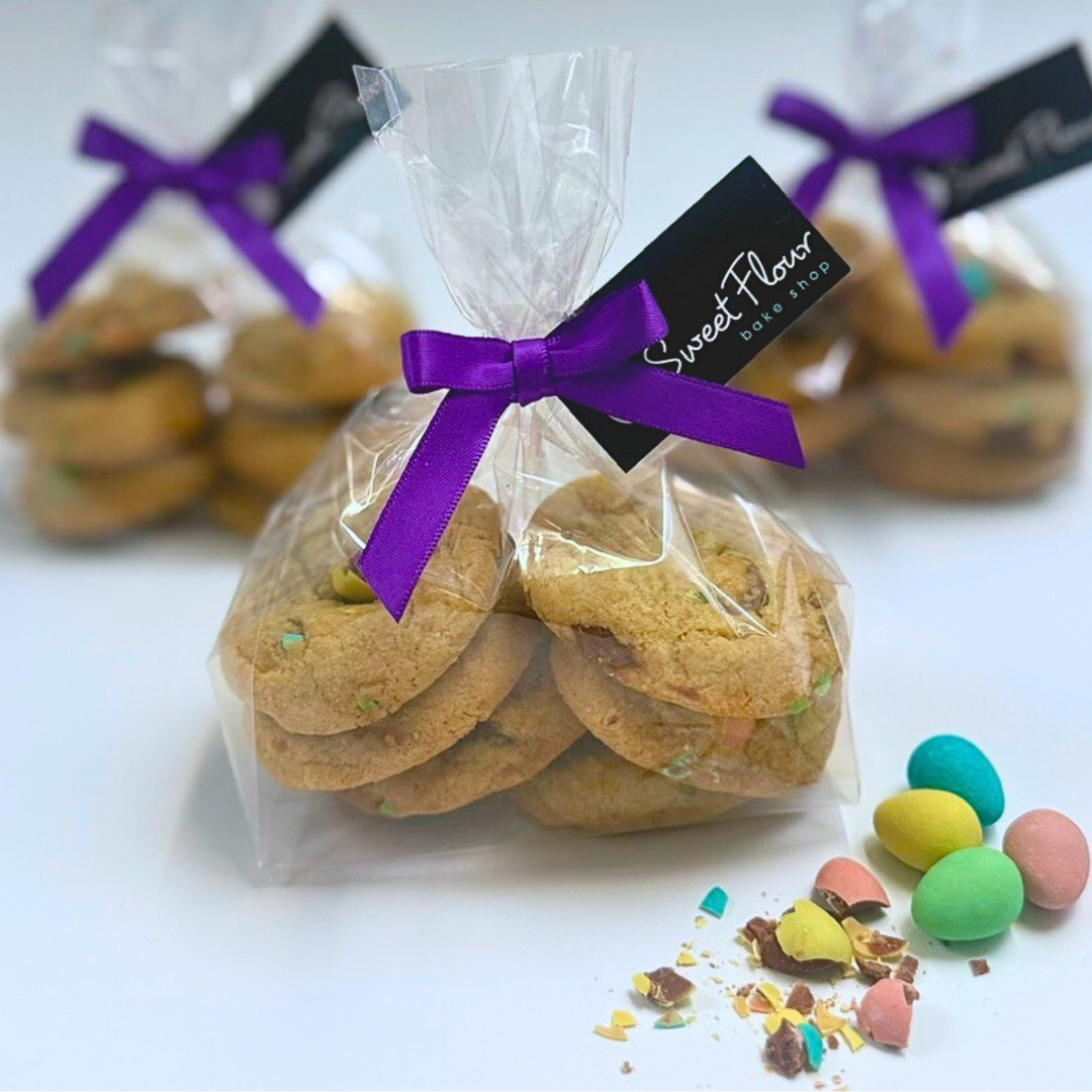 Bag of cookies with a purple bow and 'Sweet Flavor' tag, surrounded by colorful candies on a light background.
