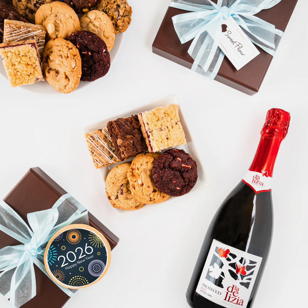 Assorted cookies, a bottle of sparkling wine, and gift boxes on a white surface.