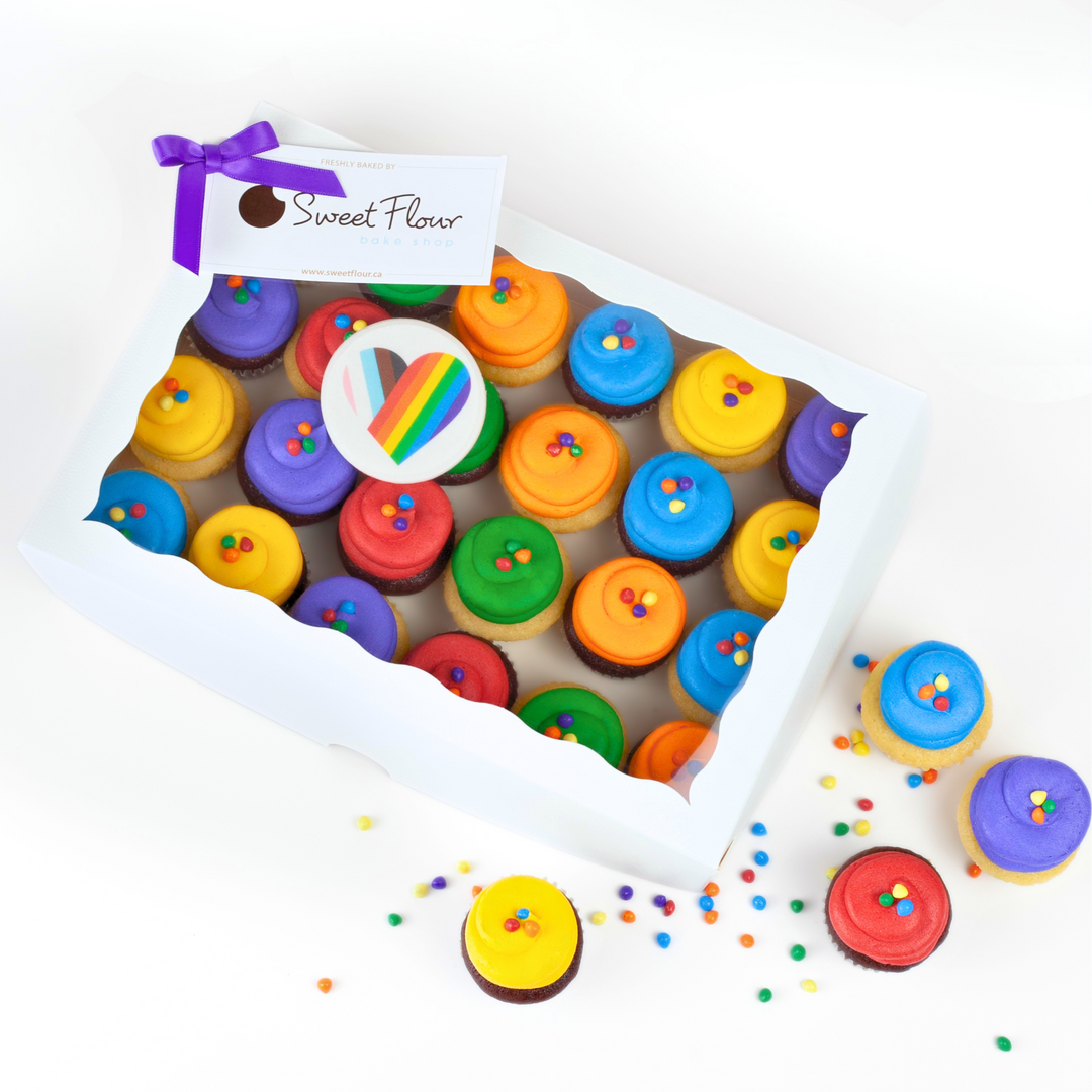 Box of colorful cupcakes with rainbow icing and a heart topper with a gift card 